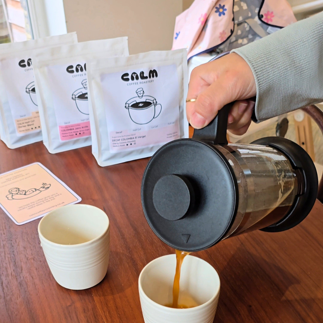 Pouring freshly brewed Calm Coffee into a cup using a French press, with specialty coffee bags and insert card in the background