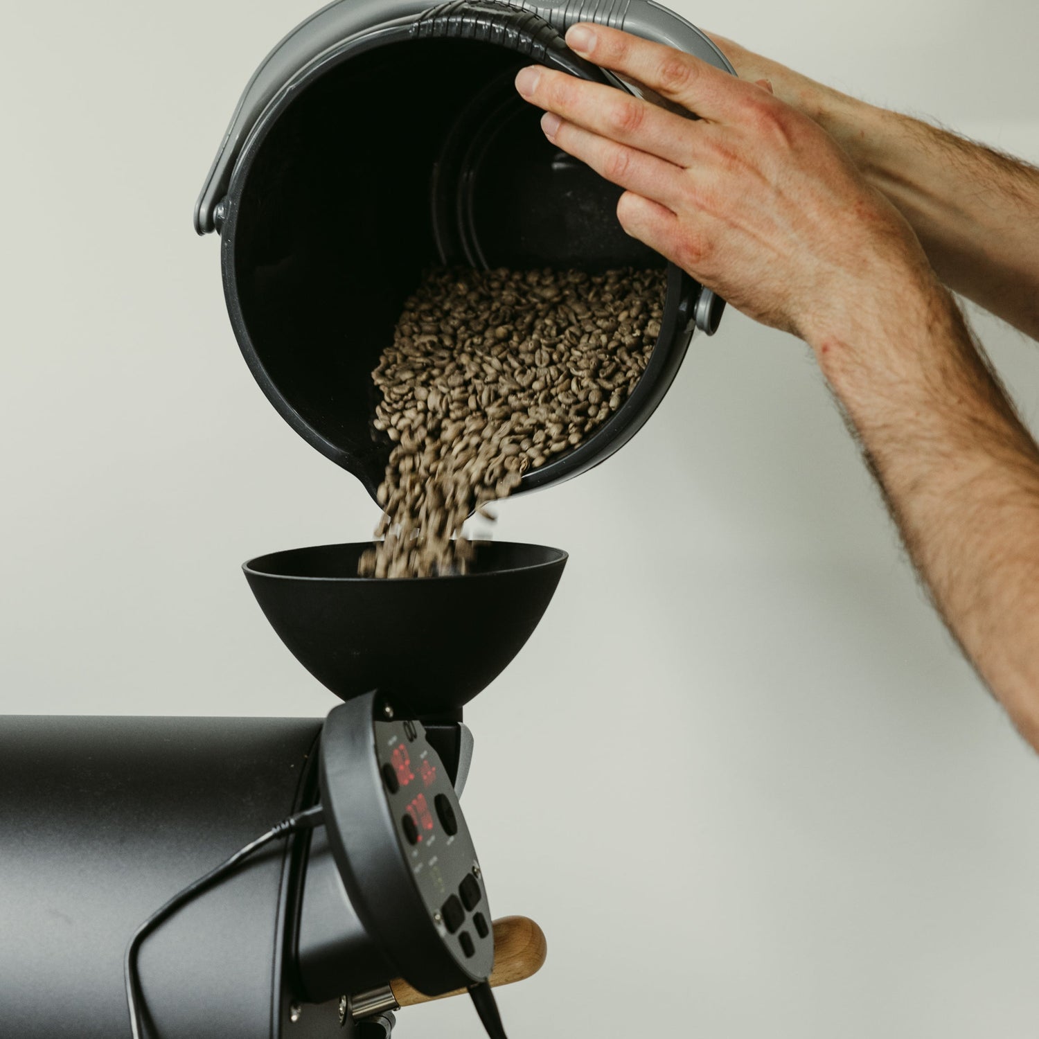 Close-up of hands pouring green coffee beans into an Aillio Bullet Coffee Roaster at Calm Coffee Roastery