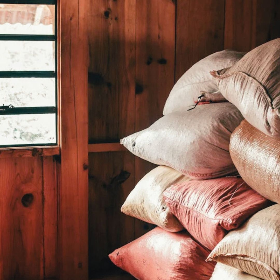 Sacks of coffee in colourful jute bags in front of a wooden wall and window.