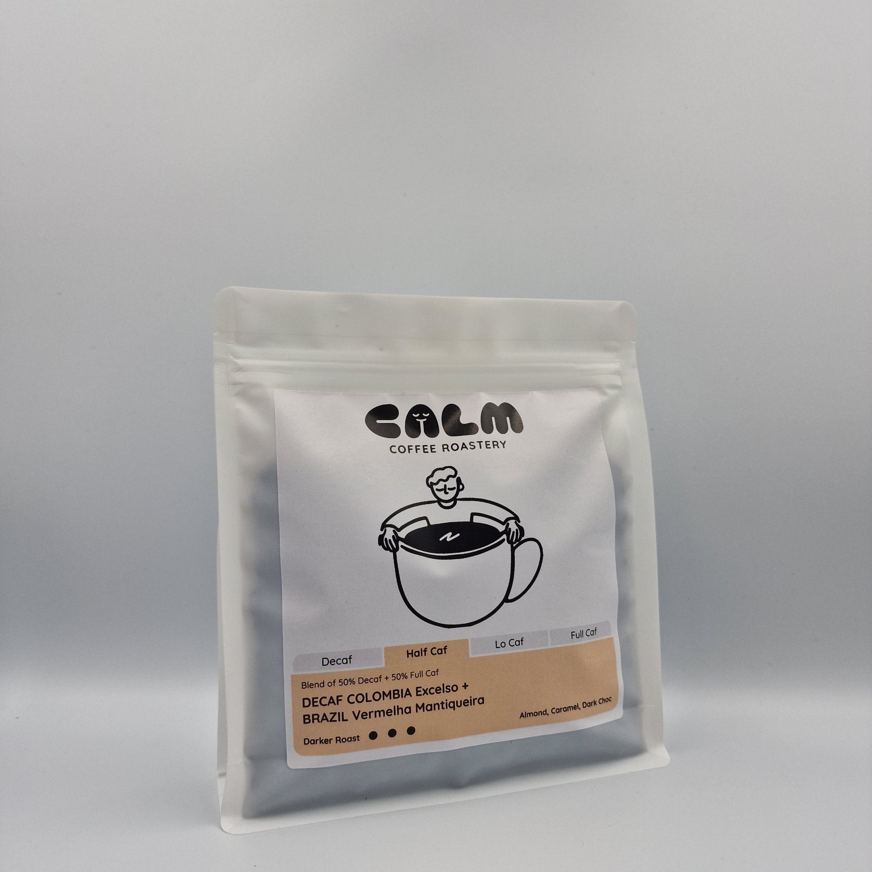 Half Caf Decaf Colombia Excelso + Brazil Vermelha coffee bag with tasting notes of almond, caramel, and dark chocolate displayed on a white background.