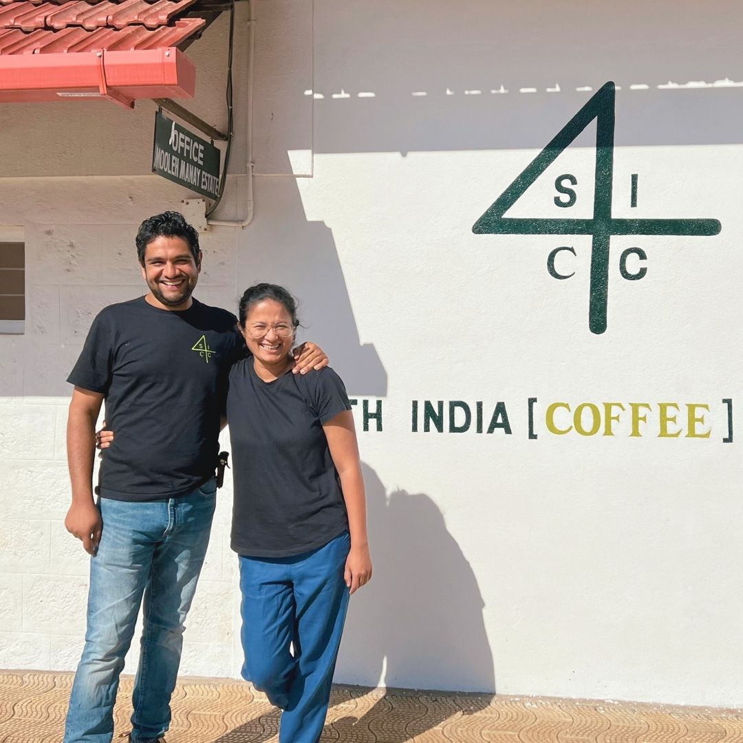 Komal and Akshay from South India Coffee Company standing in front of a building with South India Coffee Company signs.