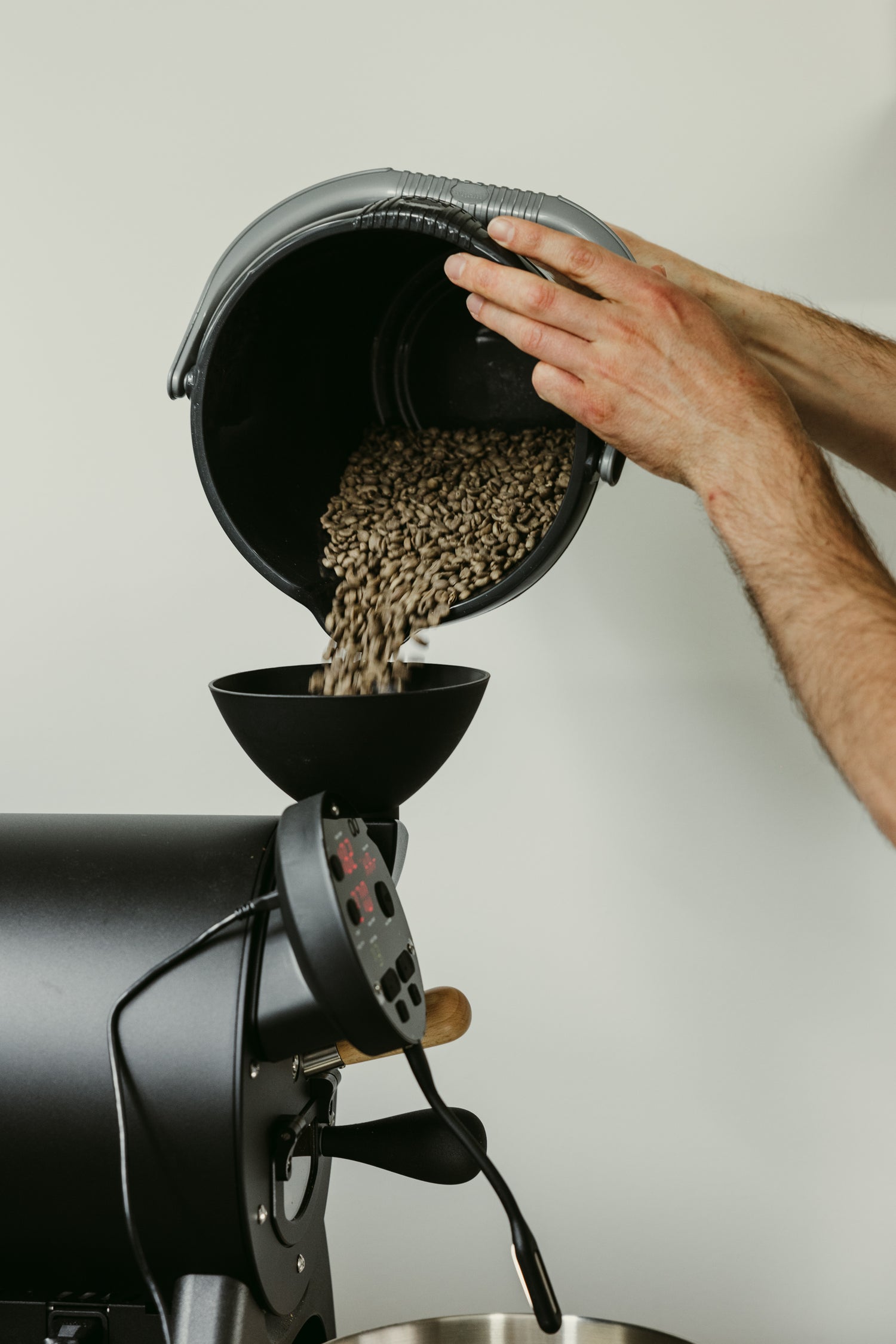 Close-up of hands pouring green coffee beans into an Aillio Bullet Coffee Roaster at Calm Coffee Roastery