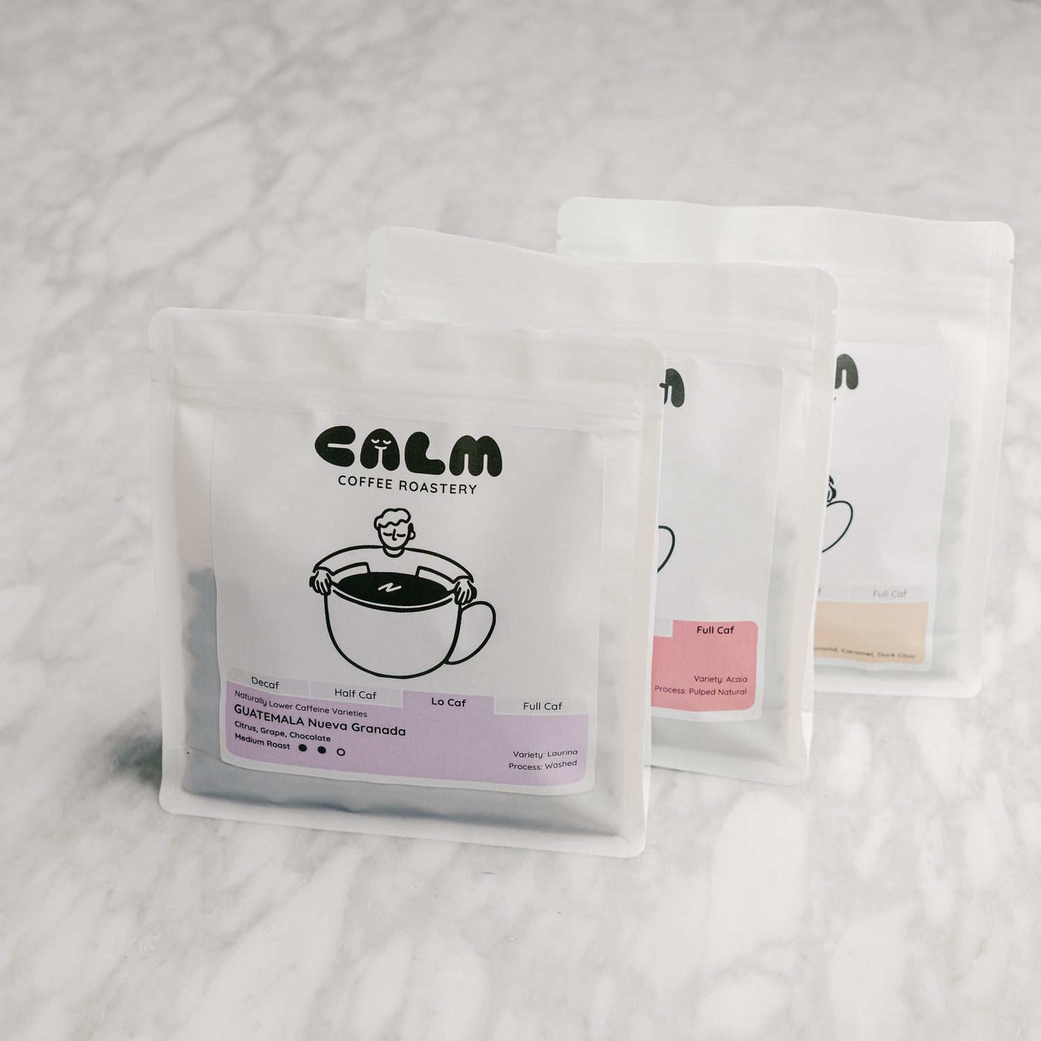 Three Calm Coffee Roastery coffee bags displayed on a marble countertop