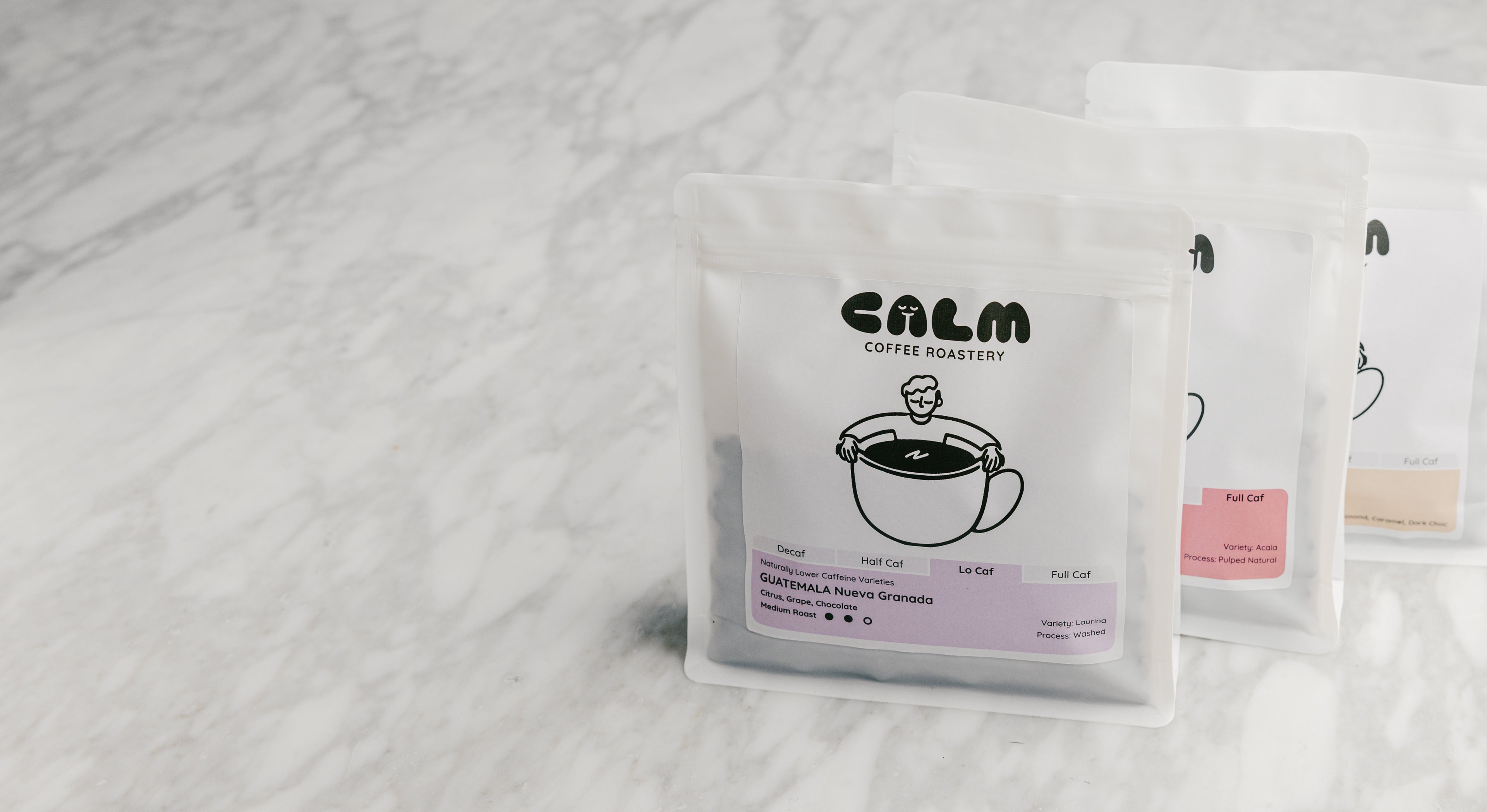 Three Calm Coffee Roastery coffee bags displayed on a marble countertop