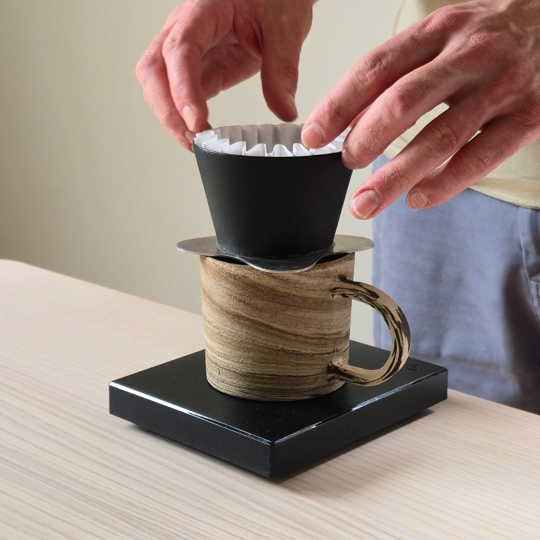 Person using a coffee brewing device with a ceramic mug on a wooden surface.