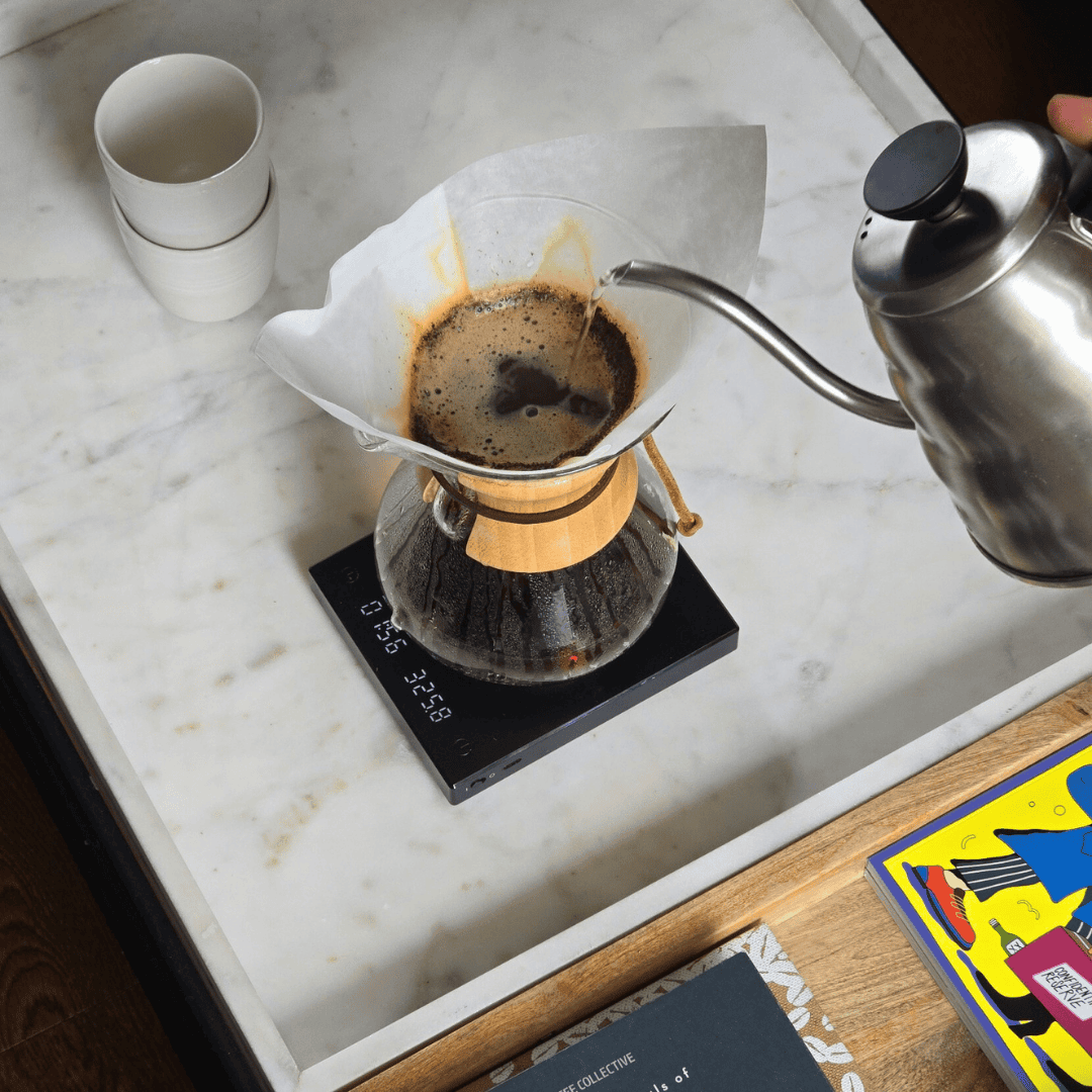 Pouring coffee from a kettle into a filter on a scale with a cup nearby.